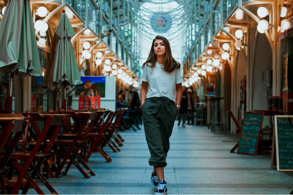 Stylish woman strolling in a chic indoor market, surrounded by shops and warm lighting.